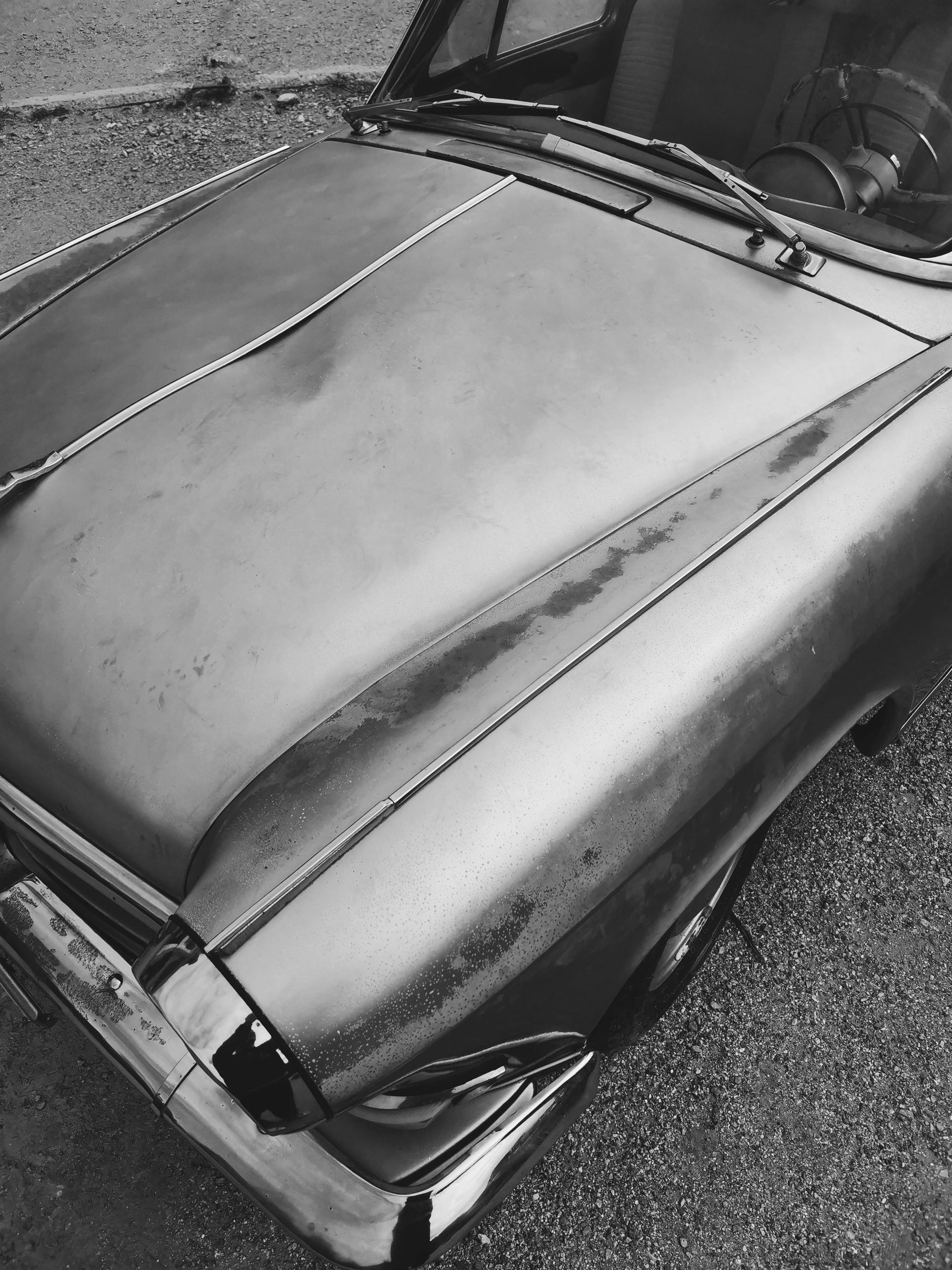 Grayscale close-up of an old car's hood, showcasing aged paint and chrome bumper.