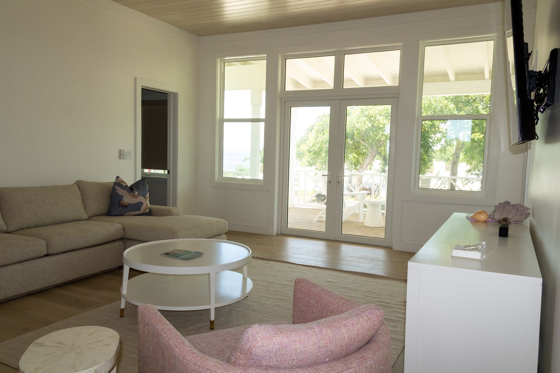 A bright living room with a couch, armchair, white coffee table, and large glass doors leading to an outdoor patio.