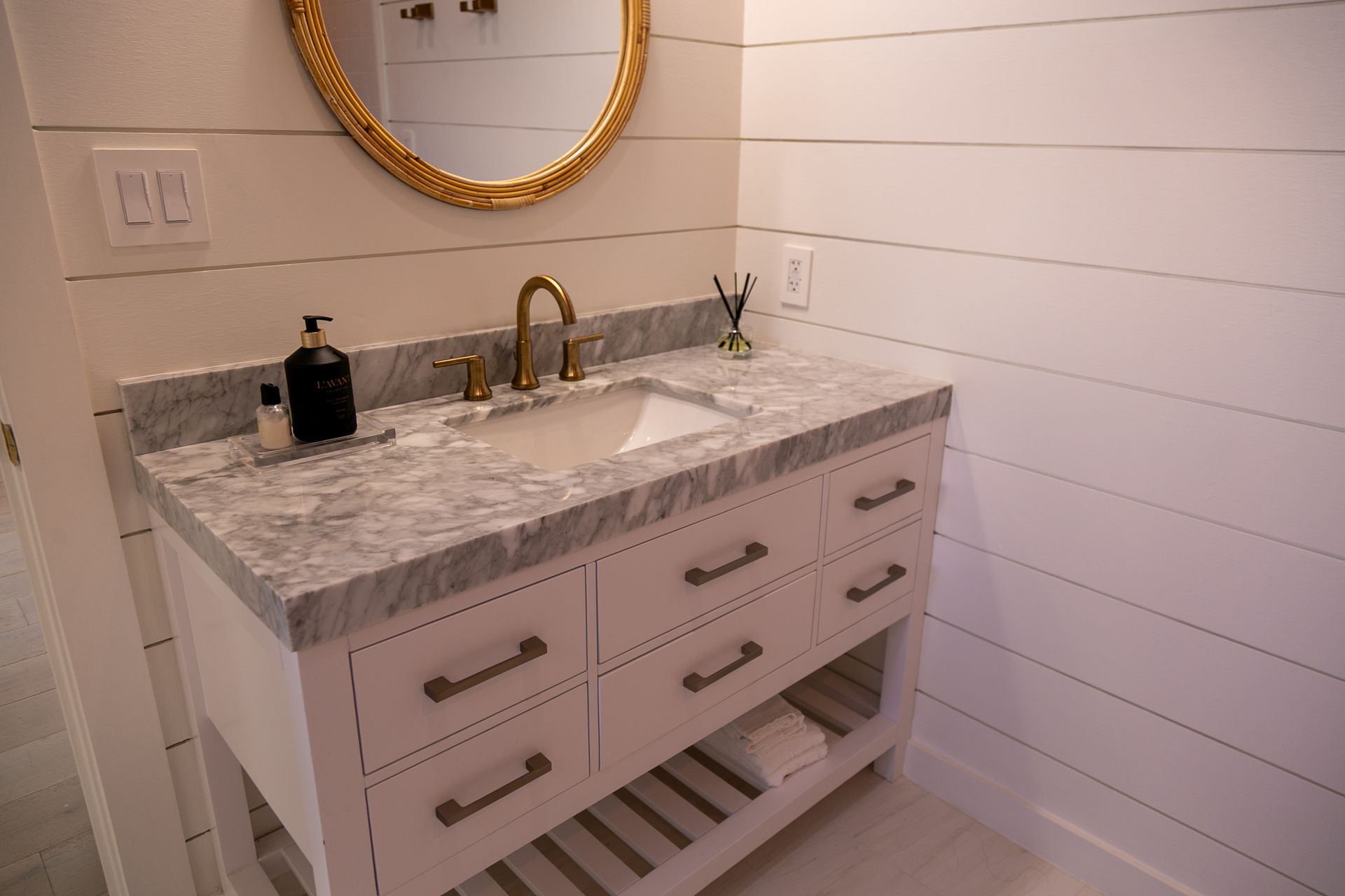 White bathroom vanity with marble countertop, gold mirror and faucet.