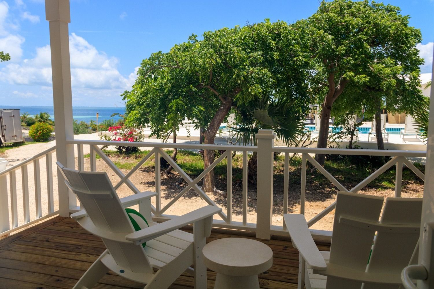 Two white Adirondack chairs on a porch overlooking trees and the ocean.