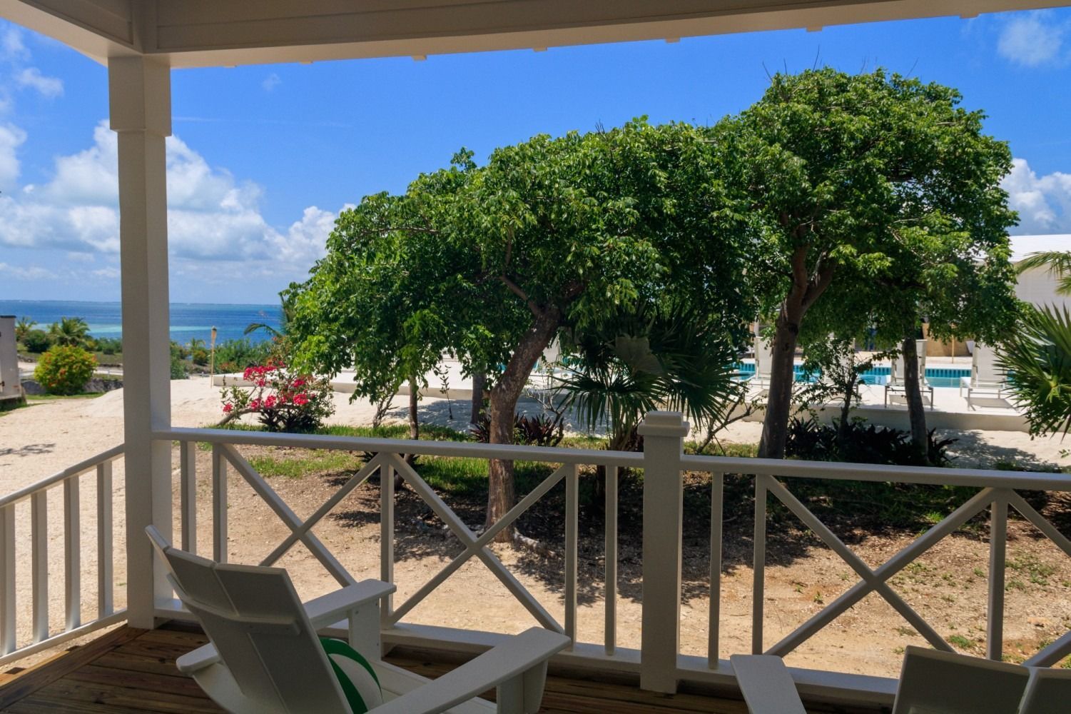 View from a porch with white chairs, trees, and blue ocean and sky.