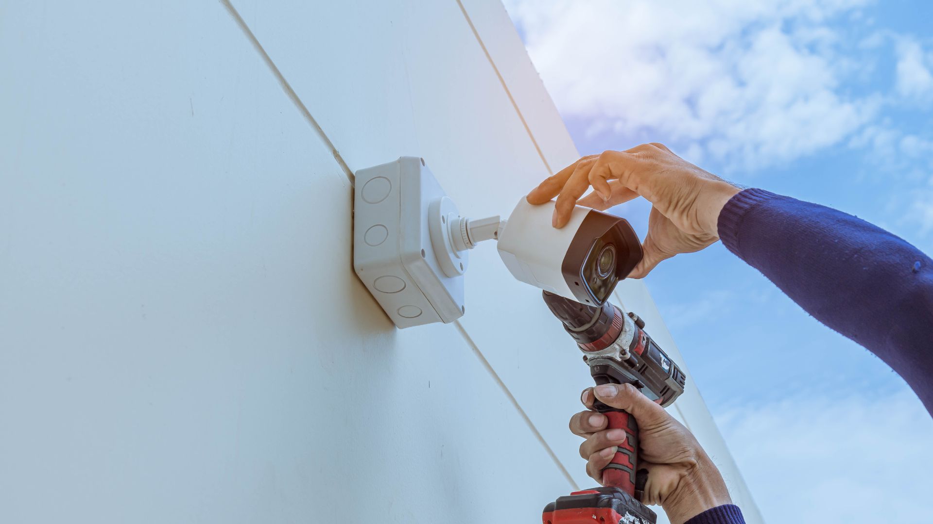 A man is installing a security camera on the side of a building.