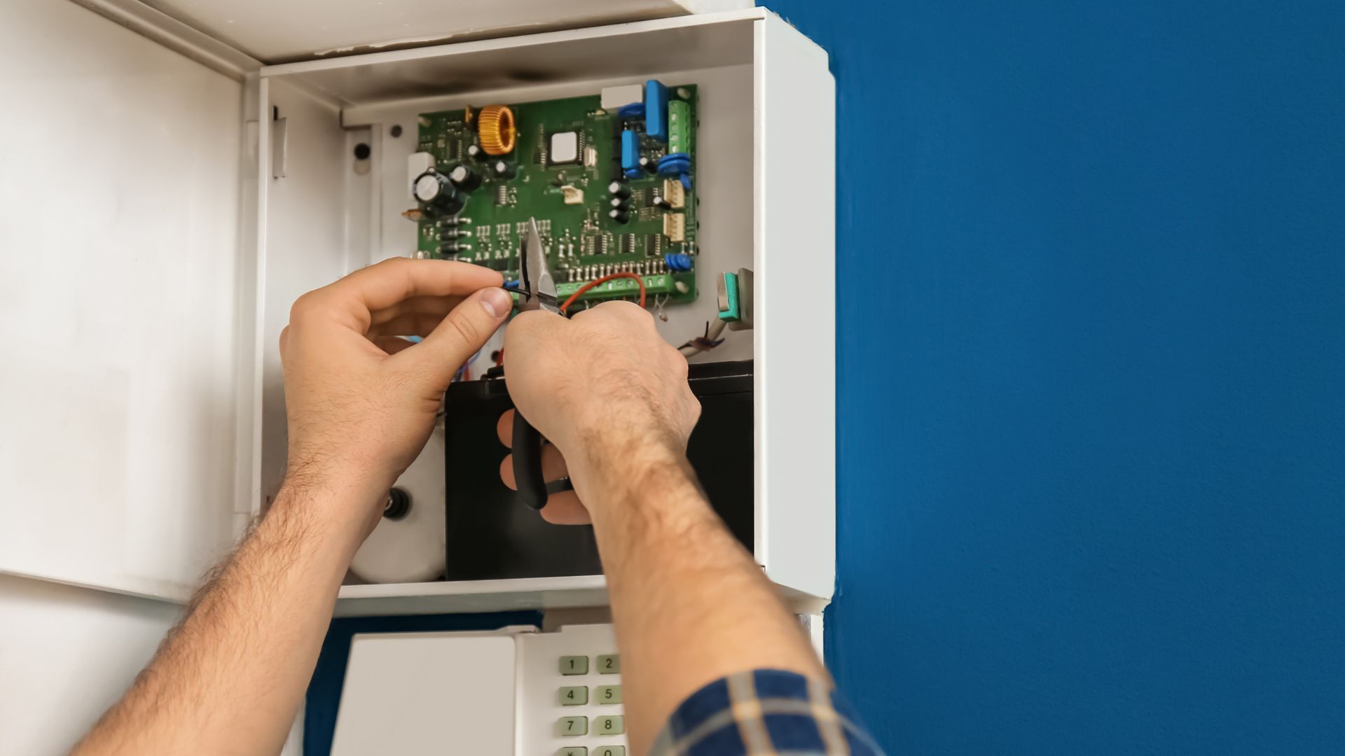 A man is fixing a security system with a screwdriver.