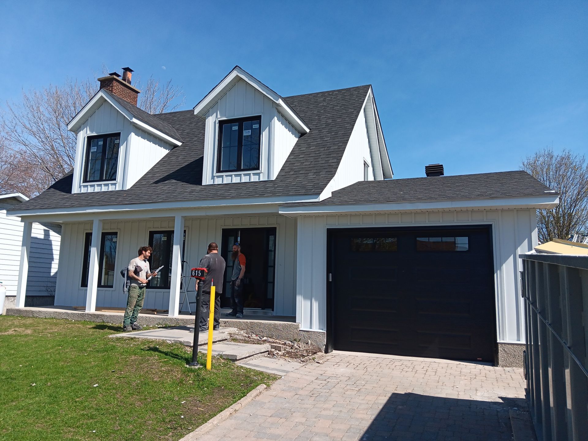 Un homme se tient devant une maison blanche avec une porte de garage noire.