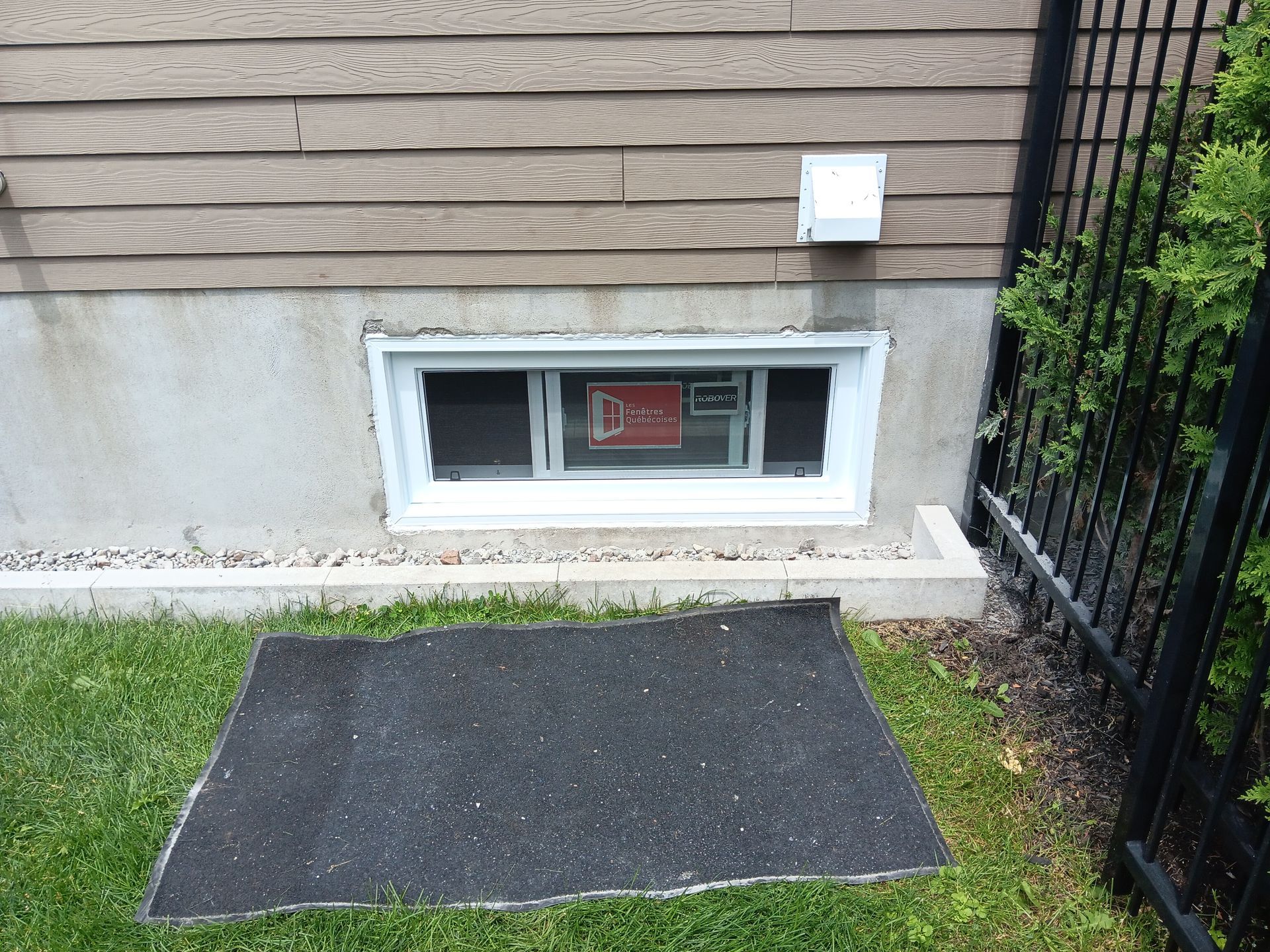 Une fenêtre sur le côté d'une maison avec un tapis noir devant elle.