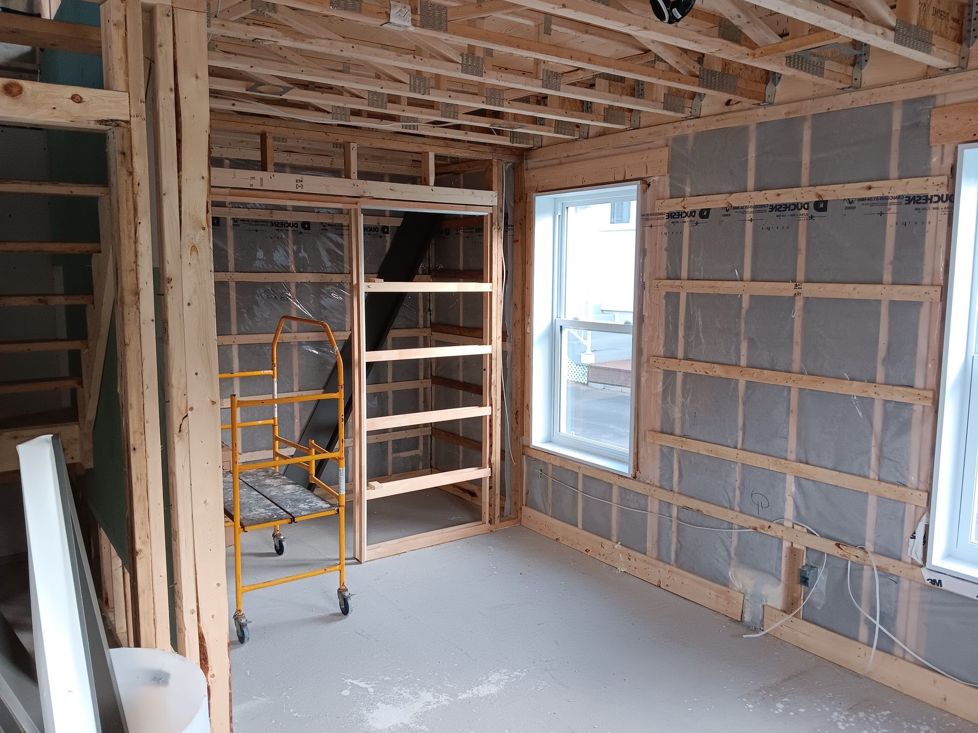 Intérieur d'une pièce en construction, avec ossature bois apparente et isolation, comportant des fenêtres et des étagères.