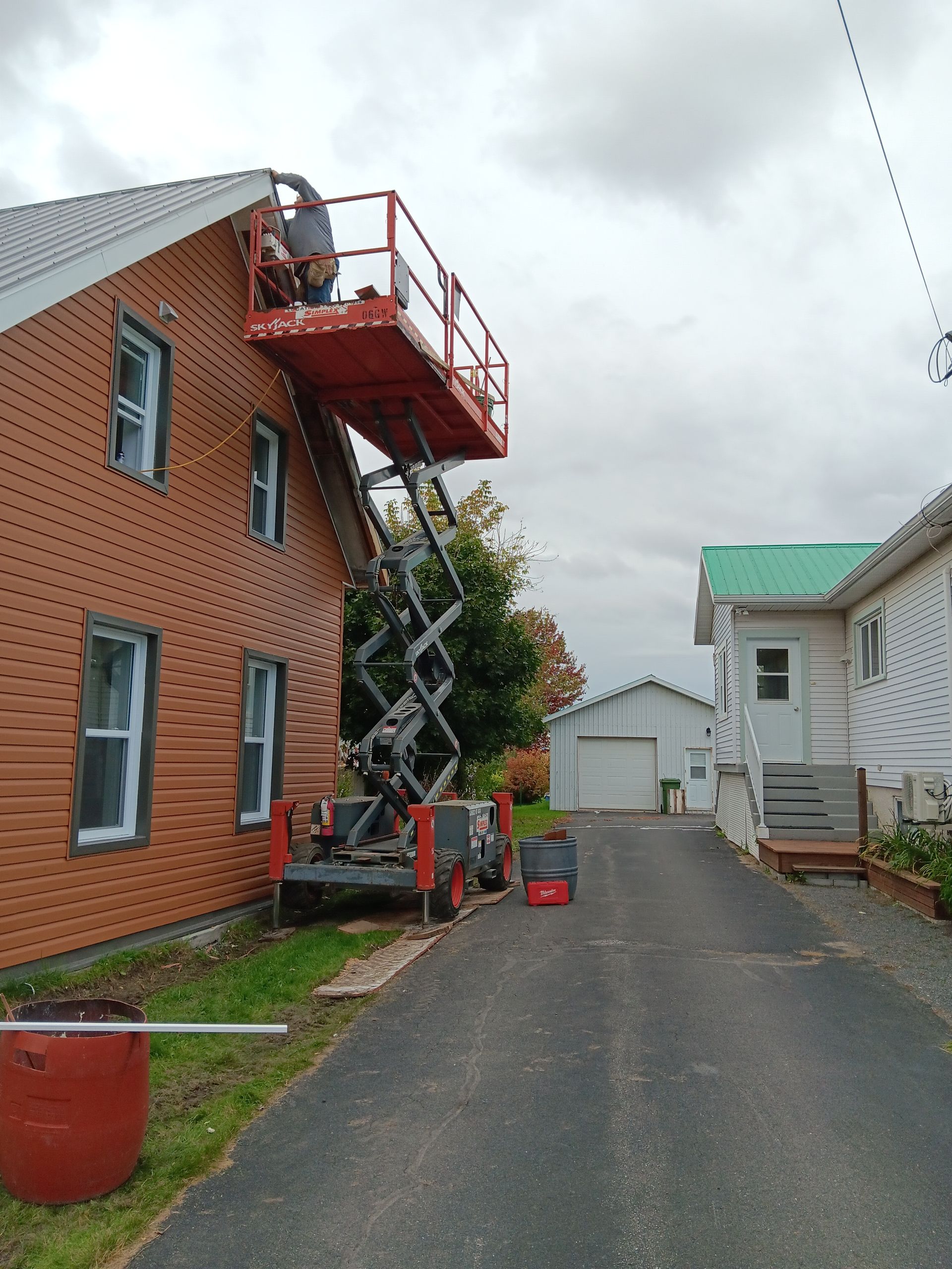 Un homme se tient debout sur un pont élévateur à ciseaux devant une maison.