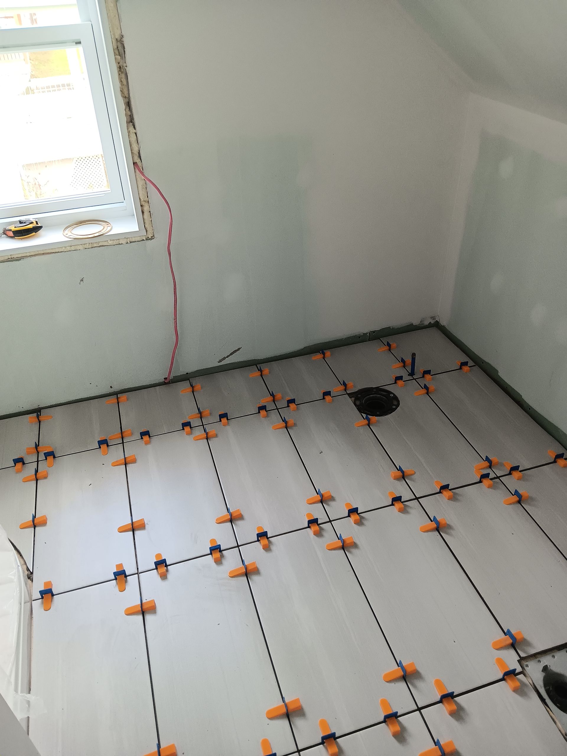 Pose du carrelage de salle de bain en cours ; carrelage posé avec entretoises de nivellement visibles.