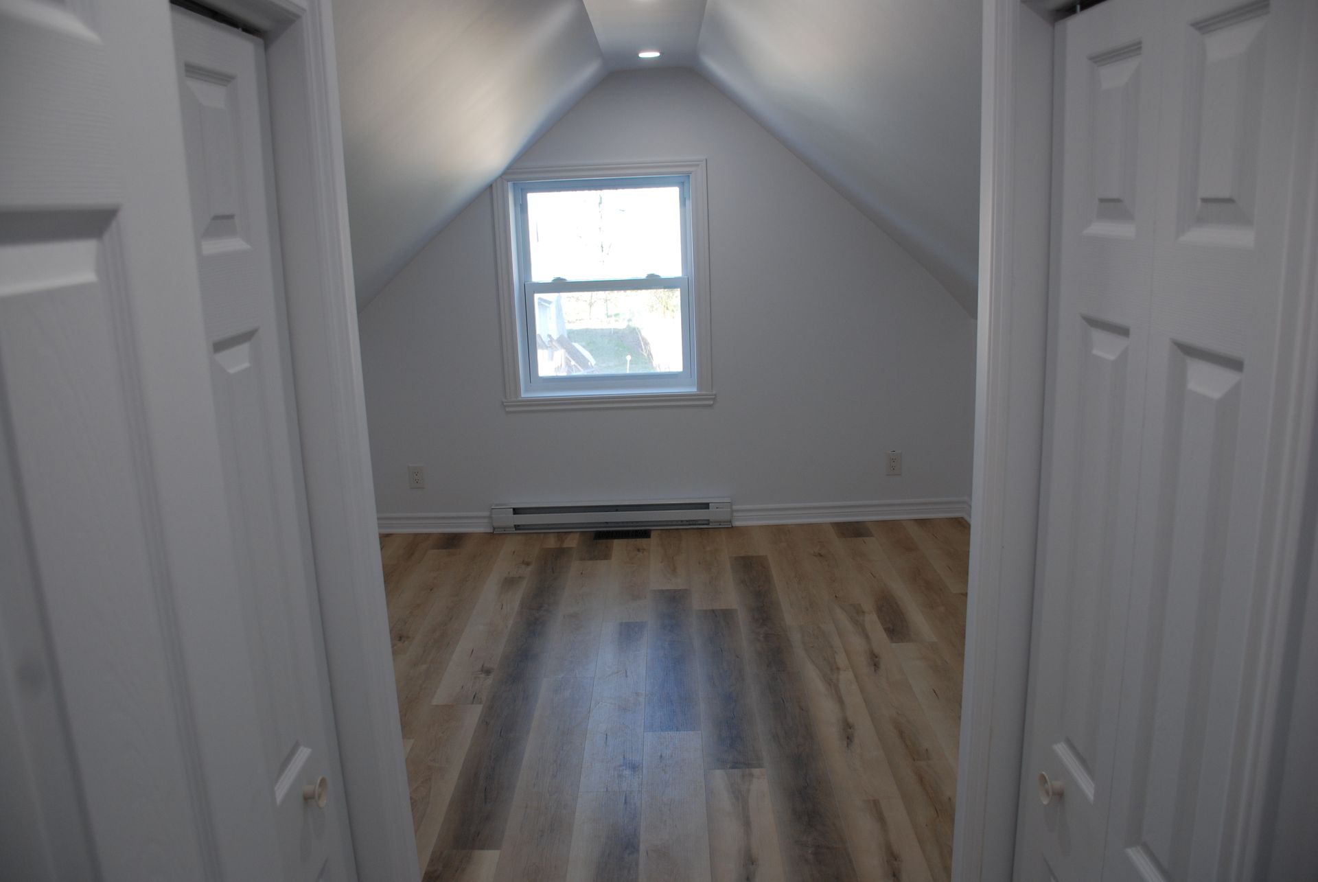 Un couloir menant à une chambre avec parquet et fenêtre.