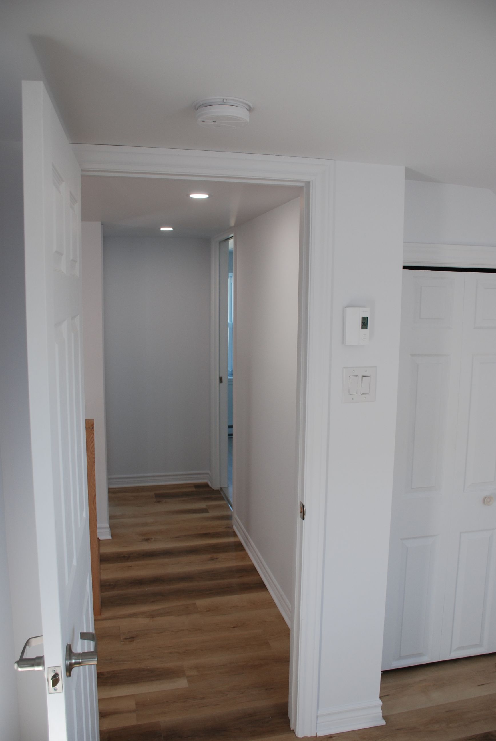 Un couloir dans une maison avec parquet et murs blancs