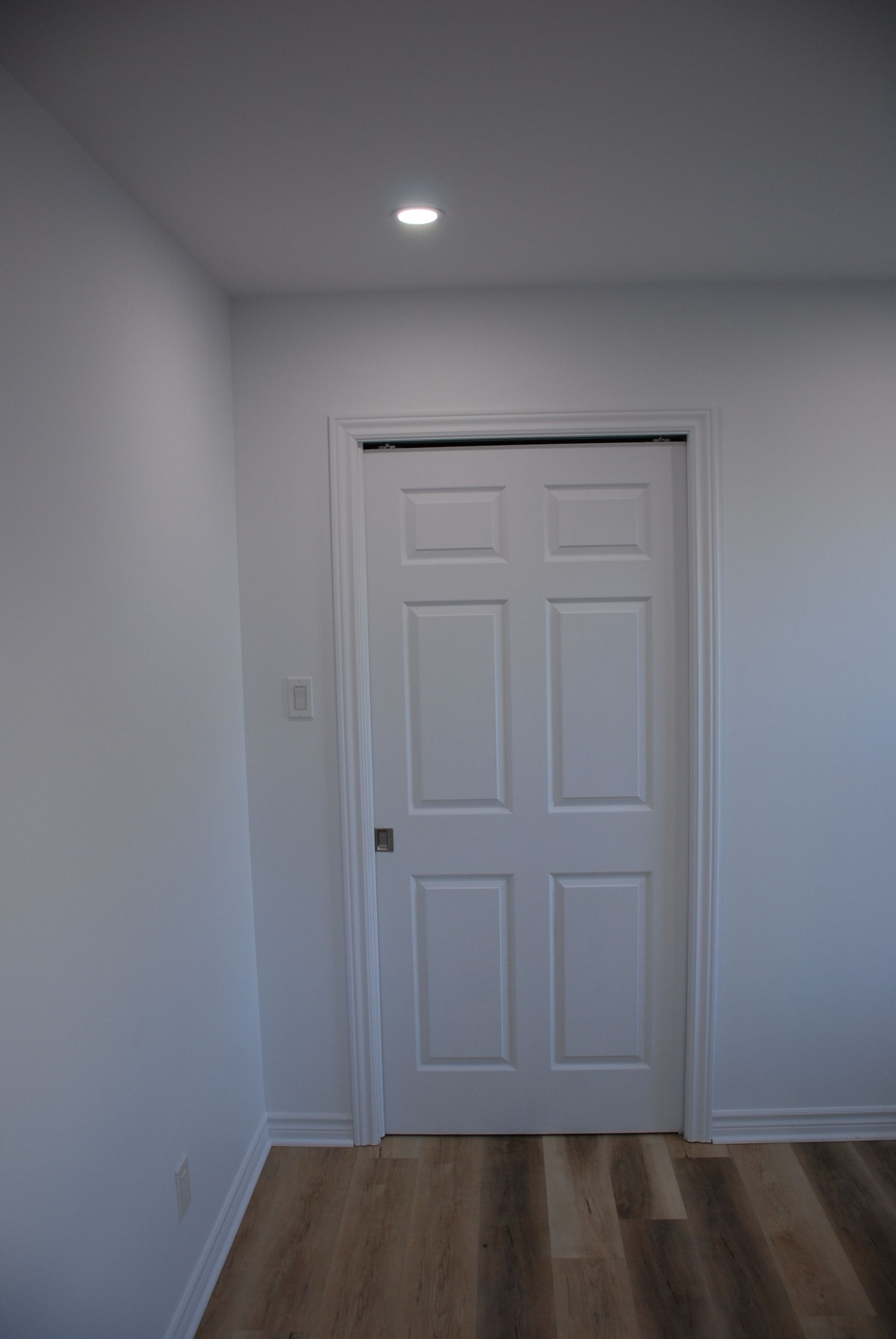 Une porte blanche dans une pièce avec du parquet et des murs blancs.