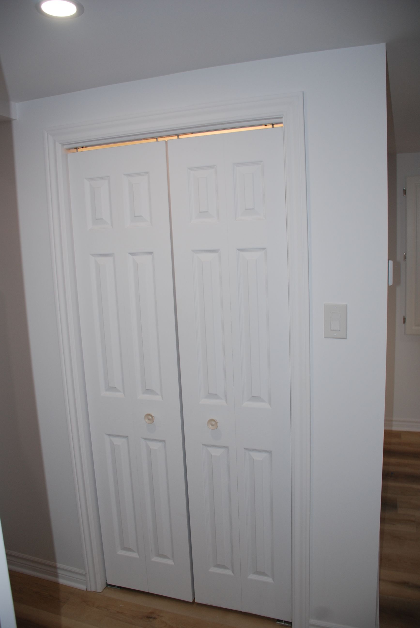 Une porte de placard blanche est ouverte dans un couloir.