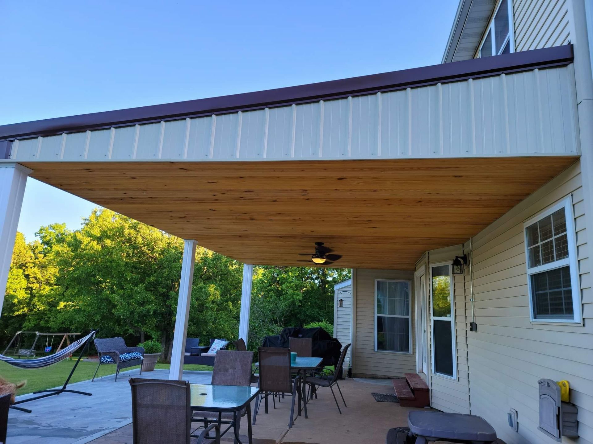 A patio with a table and chairs under a wooden roof.