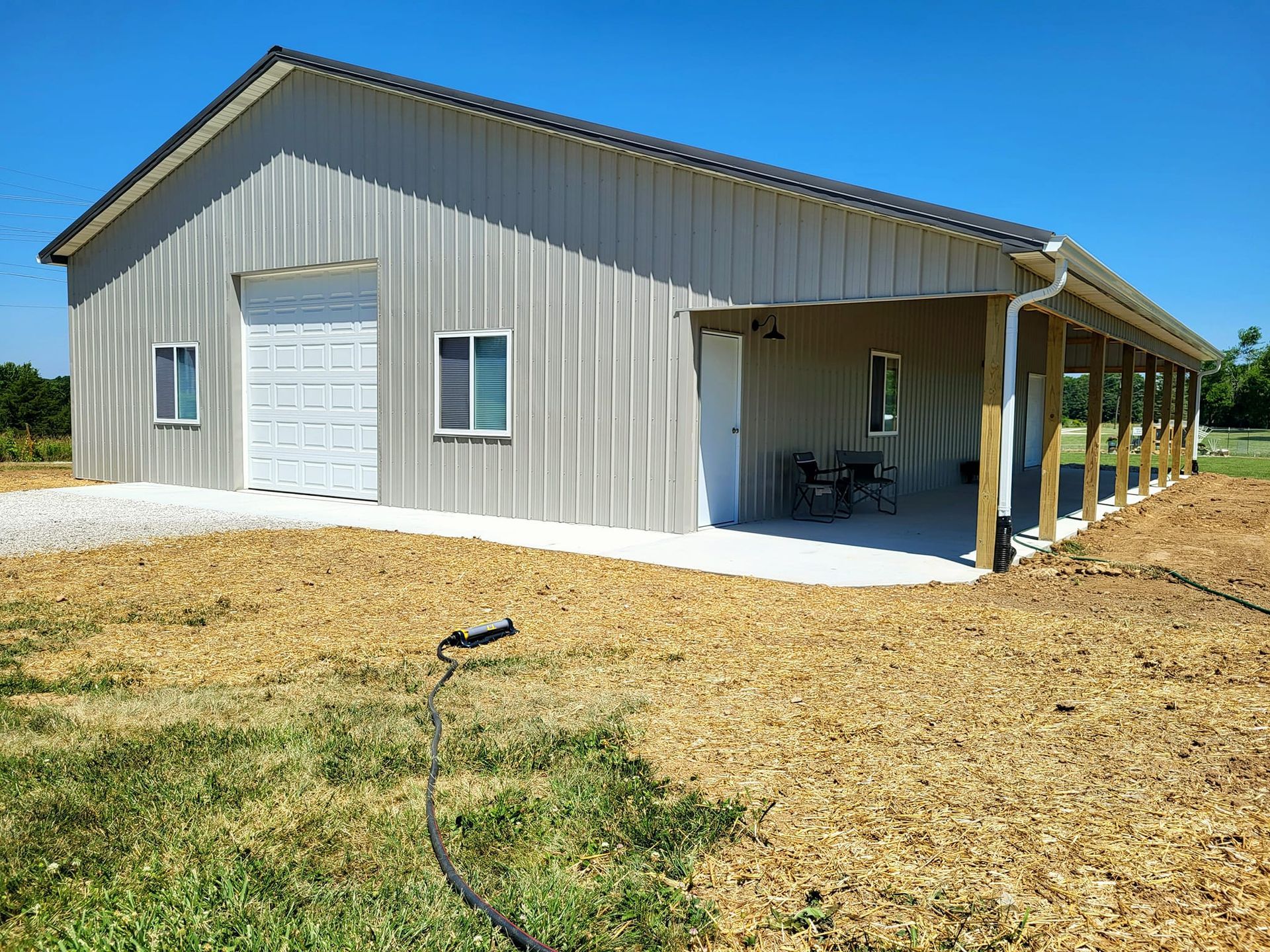 A large metal building with a porch and a hose in front of it.