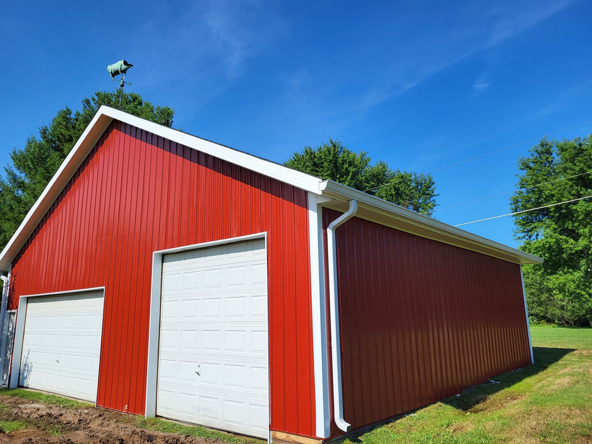 A red barn with white doors and a bird on top of it.