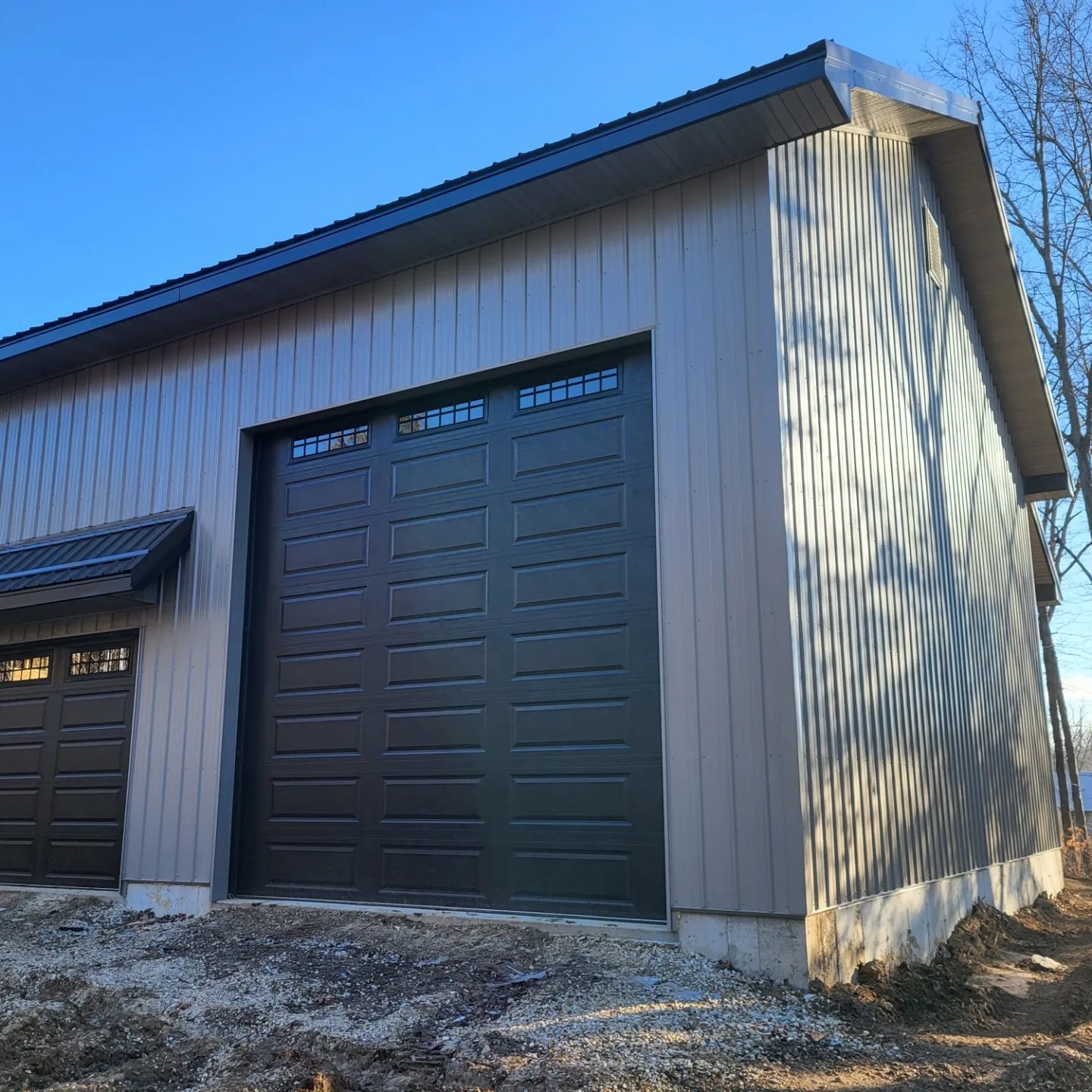 A garage with two black garage doors is sitting on top of a dirt hill.