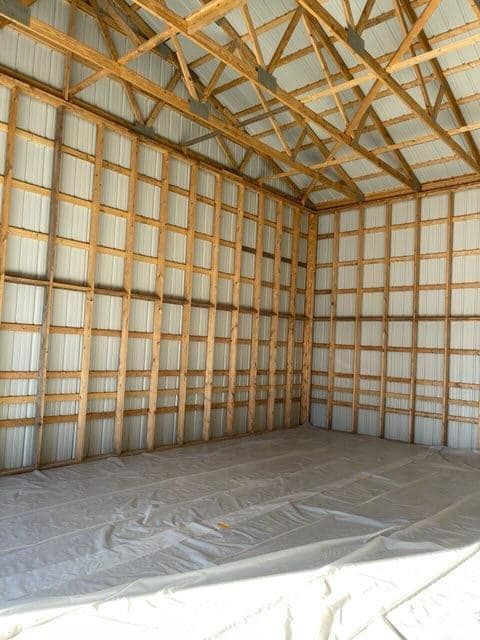 A large empty barn with wooden beams and a white tarp on the floor.