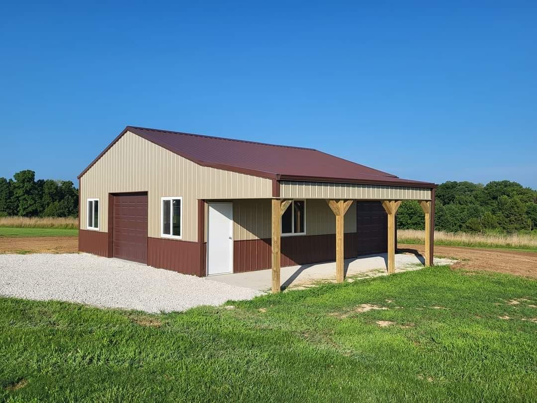 A garage with a pergola attached to it is sitting in the middle of a grassy field.