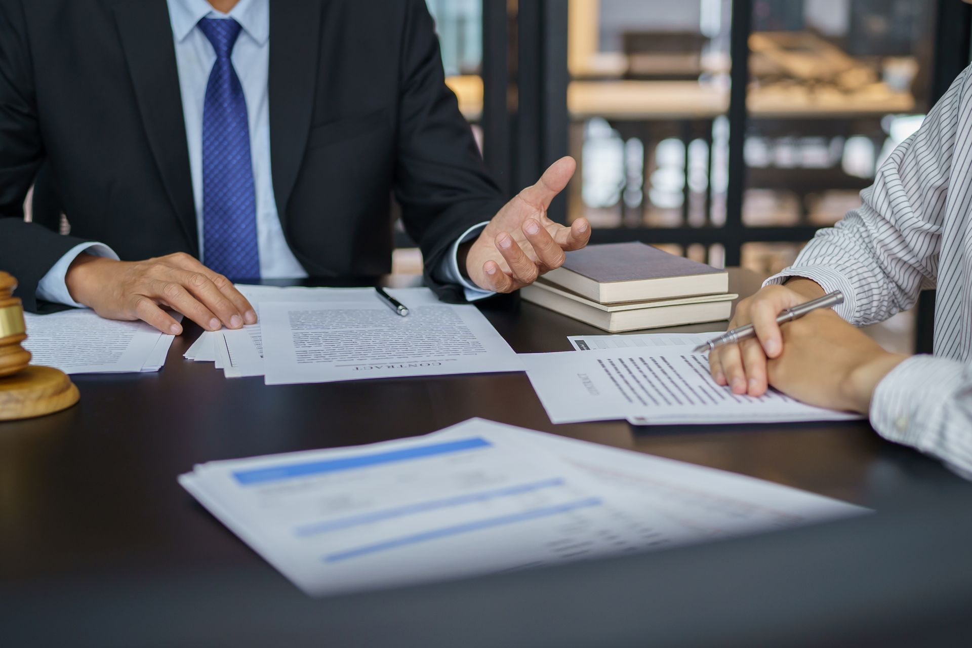 Two professionals in a business setting review legal documents and a gavel on a dark table.