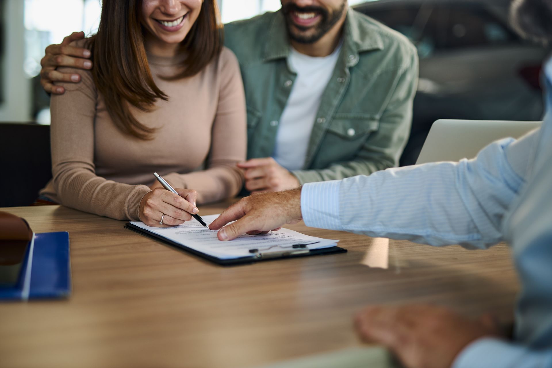A couple smiling while signing a document on a clipboard at a table, with an advisor guiding them.