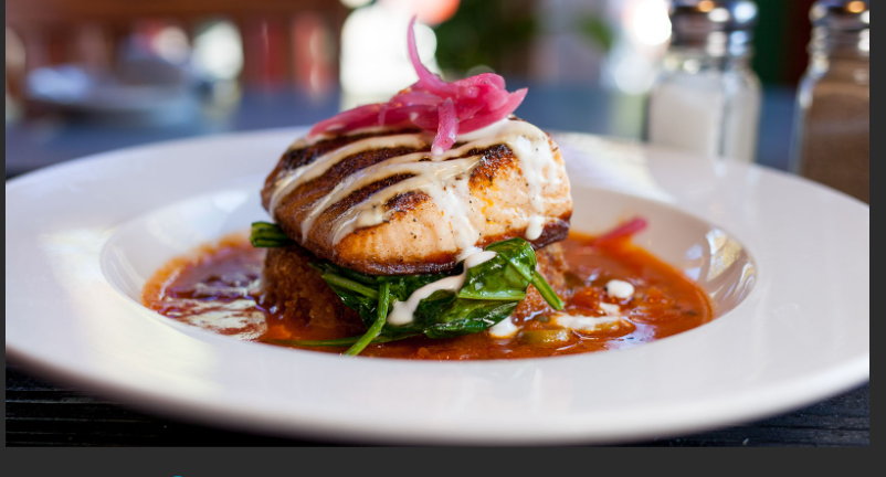 Salmon dish on a white plate with sauce, spinach, and pickled onions.