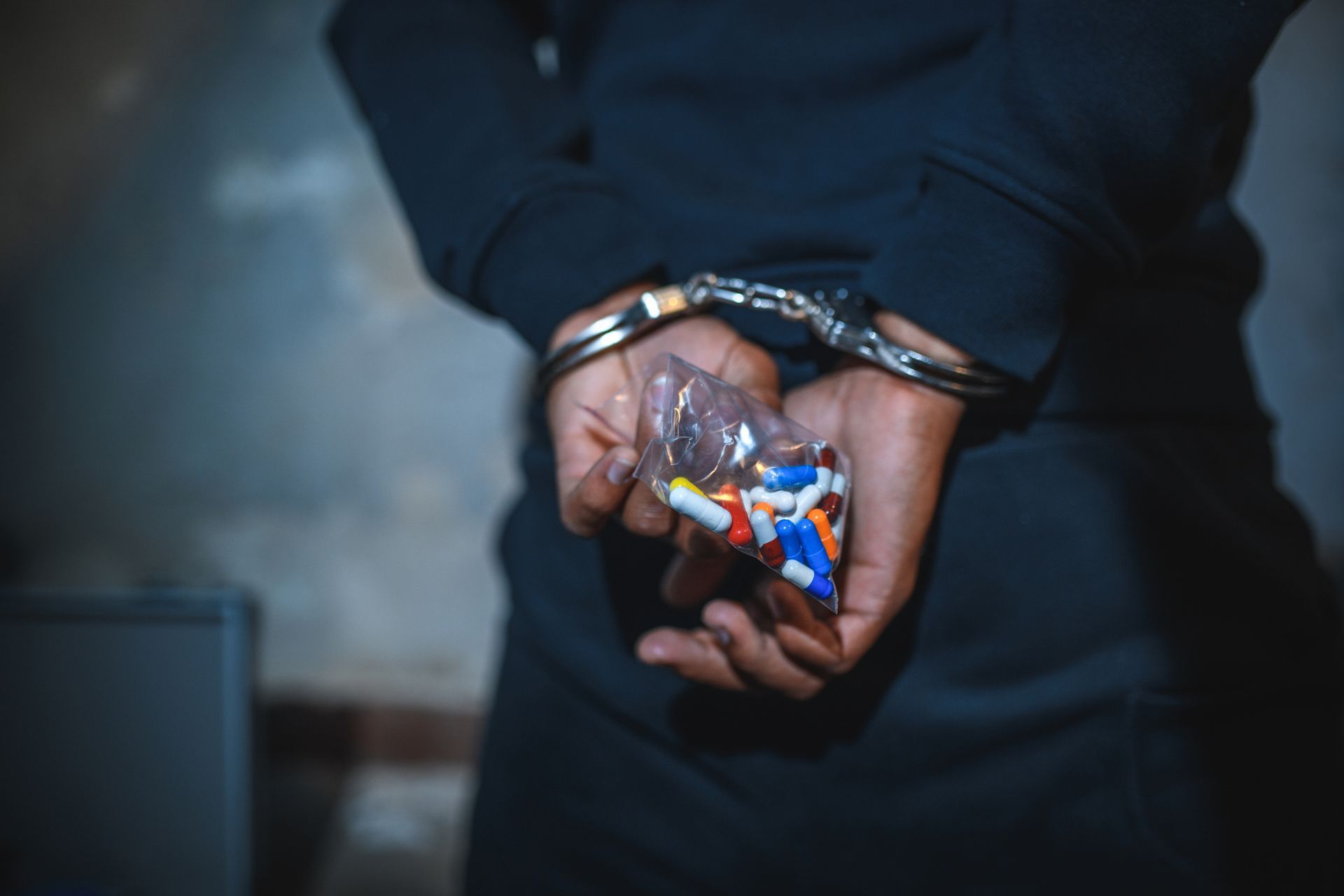 Drug charges attorney for man in handcuffs holding drugs in close-up arrest scene.