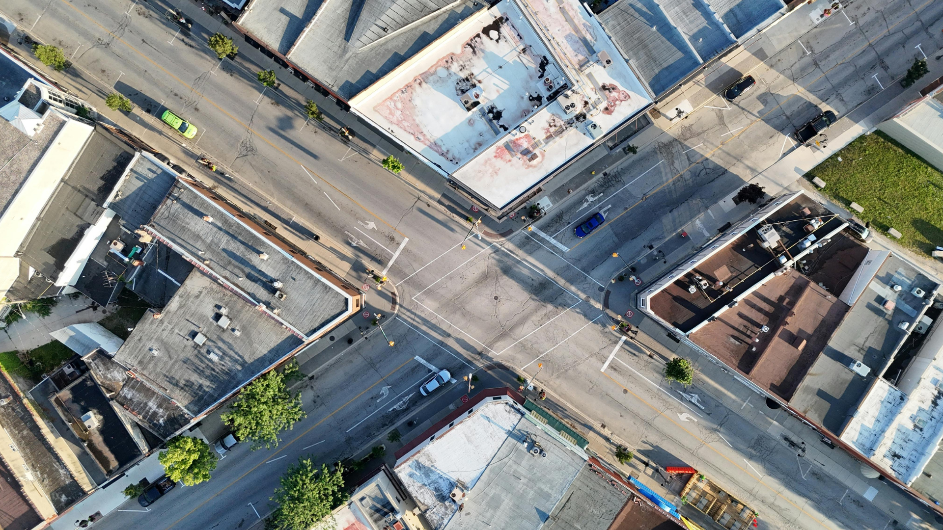 Overhead view of city intersection with buildings, roads, and crosswalks. Cars are driving on the roads.