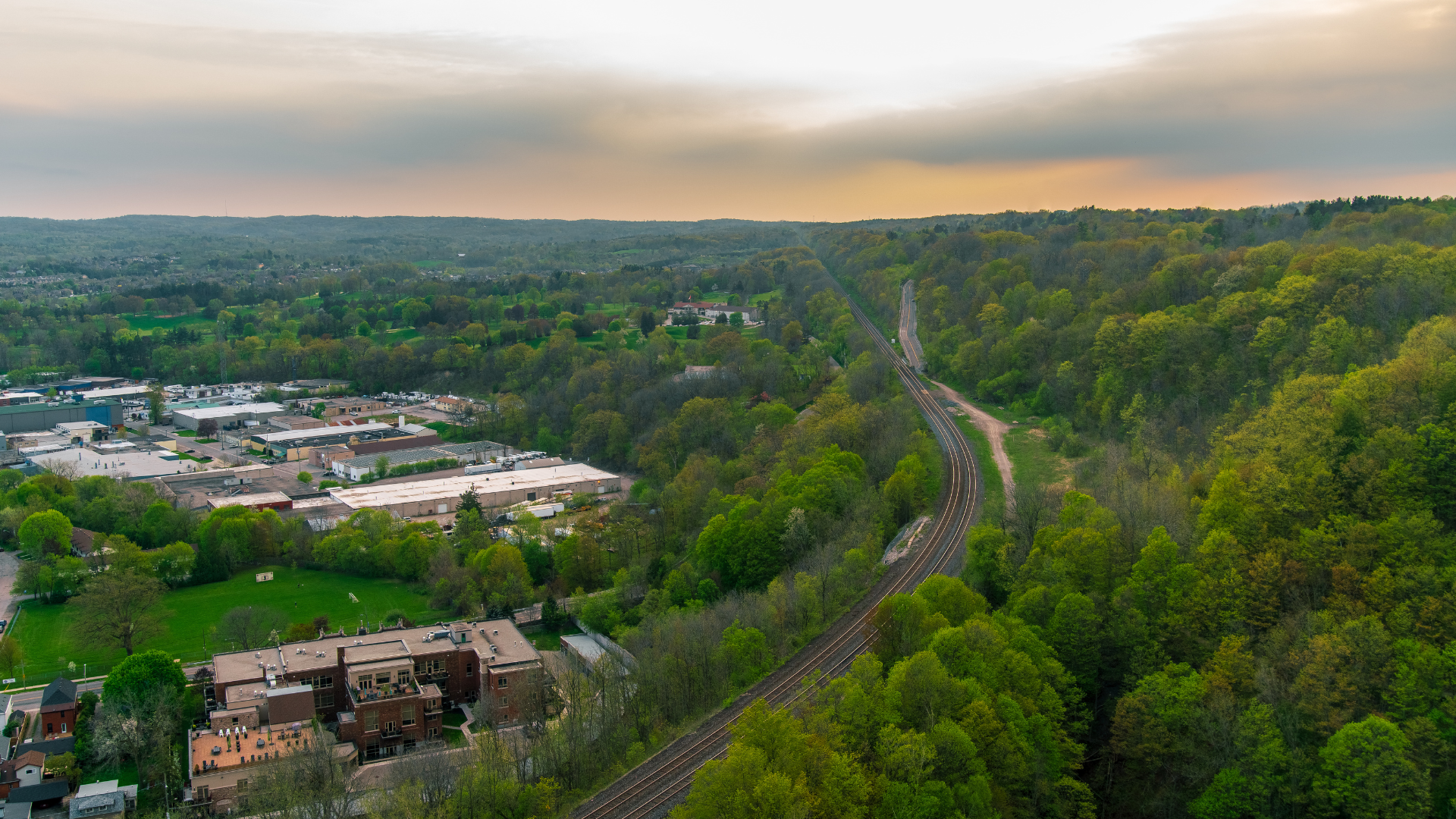 Aerial view of train tracks winding through a green, forested valley, with a small town at the edge.