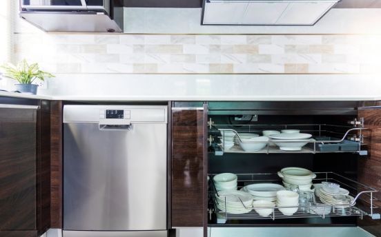 Stainless steel dishwasher next to a pull-out cabinet holding white dishes in a modern kitchen.