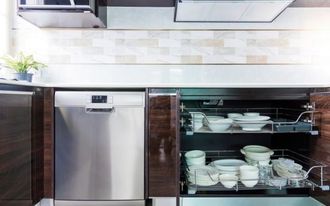 Stainless steel dishwasher next to a pull-out cabinet holding white dishes in a modern kitchen.