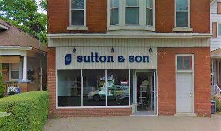 Sutton & Son storefront with large windows, white door, and red brick building.