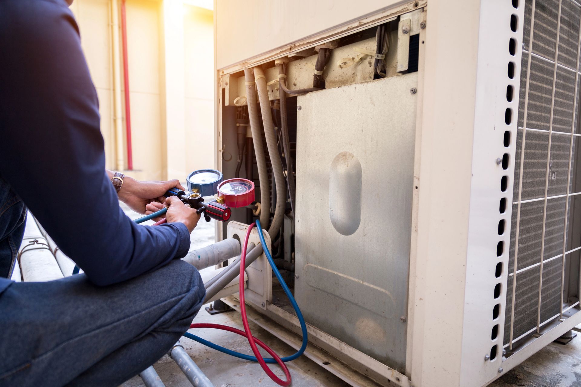 Técnico utilizando manómetros para dar mantenimiento a una unidad exterior de climatización con paneles expuestos y mangueras conectadas.