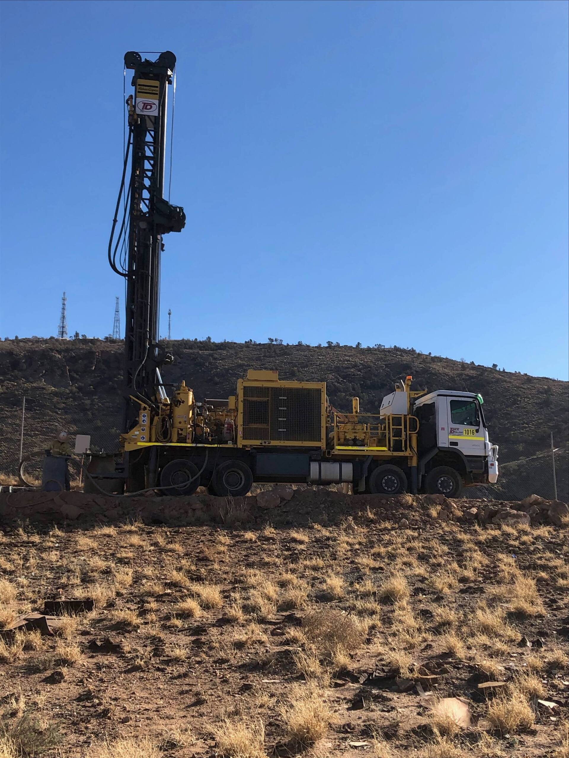 Yellow and black drilling rig on a truck in a desert setting under a clear blue sky.