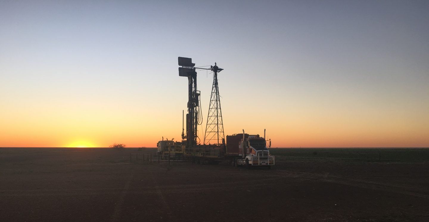 Drilling rig at sunset in a field with a vibrant orange sky.