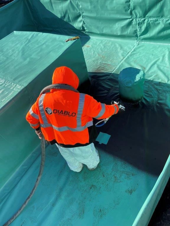 A man in an orange jacket is spraying something on a blue surface.  | Oakland, CA  | Diablo Roofing