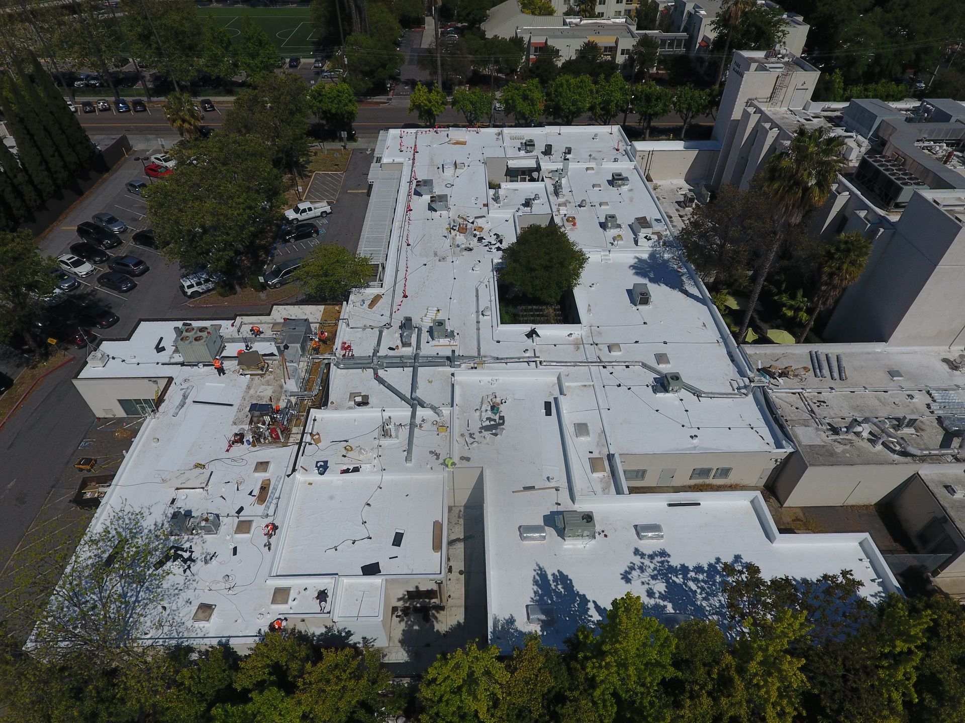 An aerial view of a large building with a white roof surrounded by trees.  | Oakland, CA  | Diablo Roofing