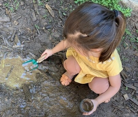 A little girl is playing in the mud with a shovel.