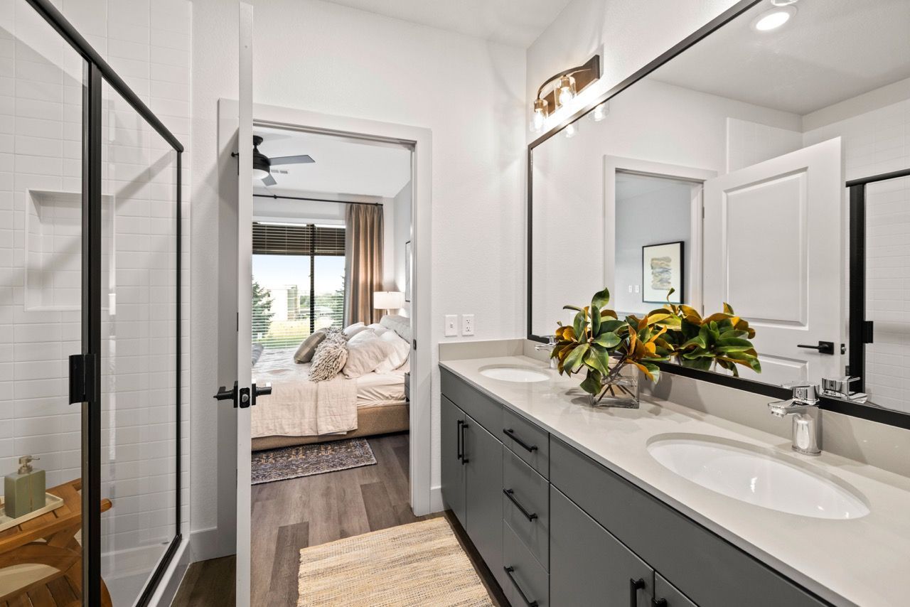 Modern apartment bathroom with a double-sink vanity, large mirror, and glass-enclosed shower.