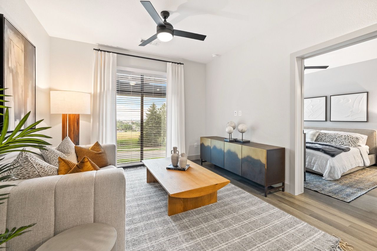 Bright living room with beige sofa, wooden coffee table, and doorway to the bedroom.