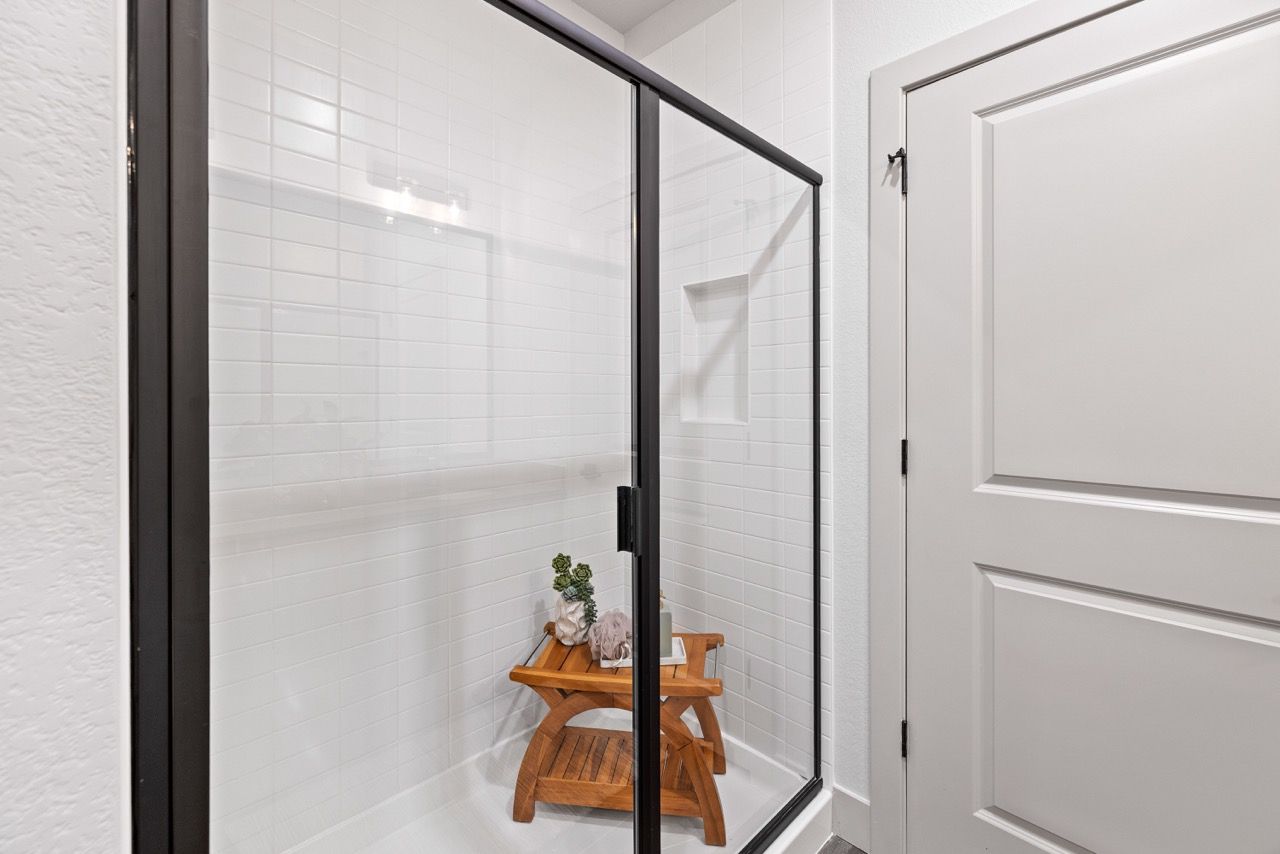 Glass-enclosed shower with white tile walls in a compact apartment bathroom.