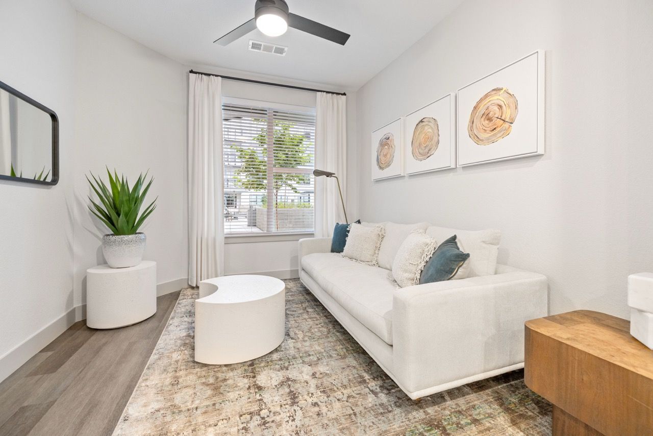 Modern apartment living room with a white sofa, round white coffee table, potted plant, and triptych wall art.