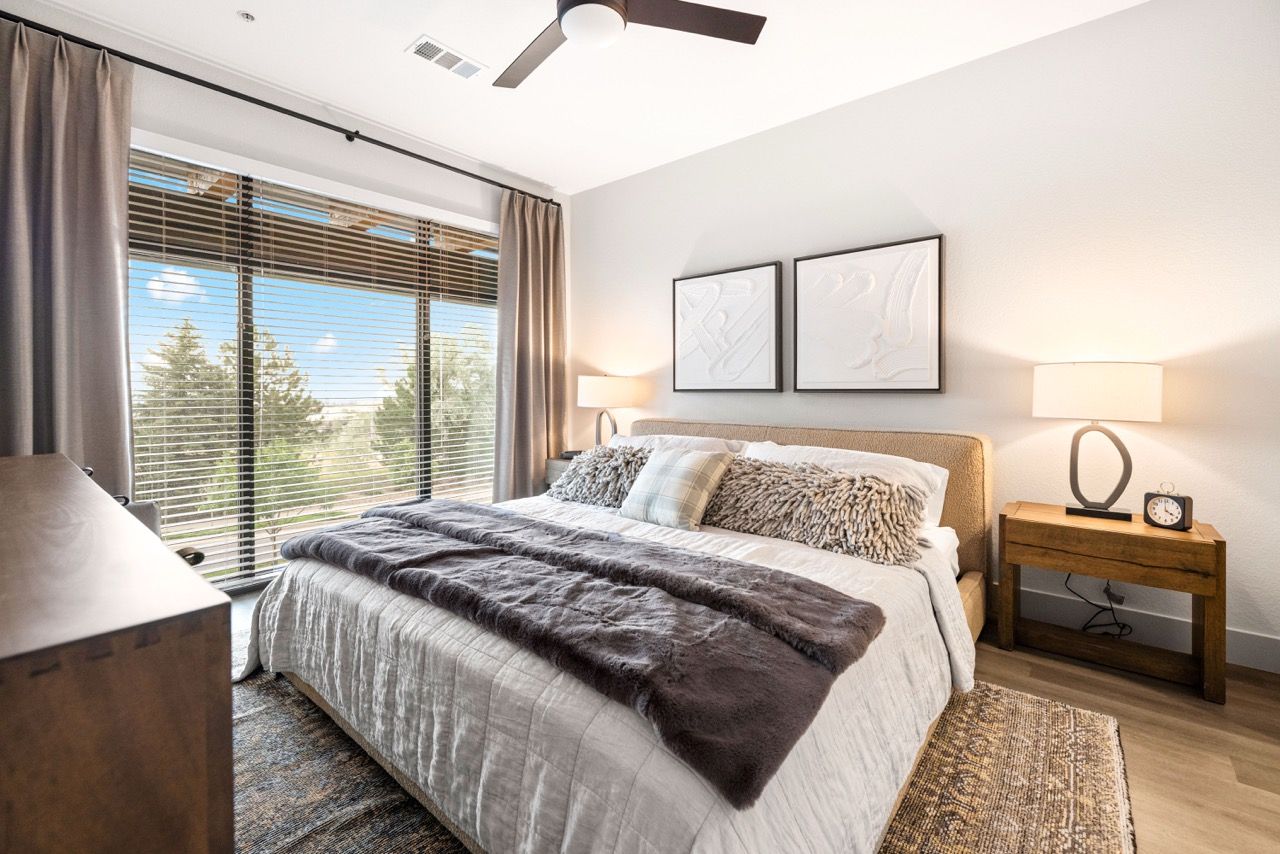 Bright bedroom with a large window, blinds, and two nightstands.