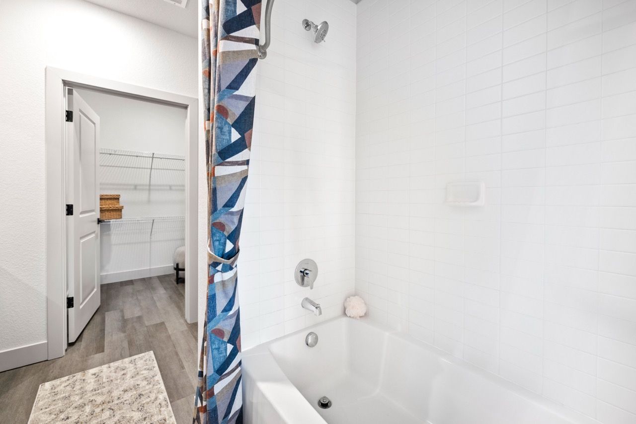 Bright bathroom with white tiled shower/tub, chrome fixtures, and a colorful geometric curtain.