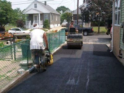 A man is pushing a roller down a road in front of a house