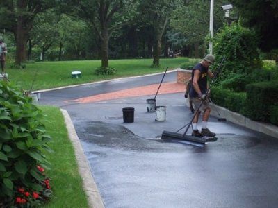 A man is painting a driveway with a broom
