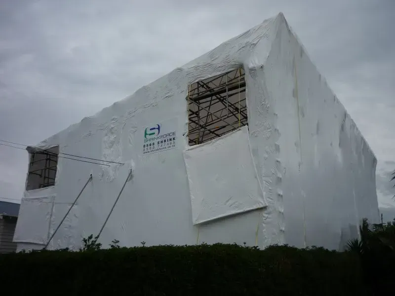 A large white building is covered in plastic and scaffolding.