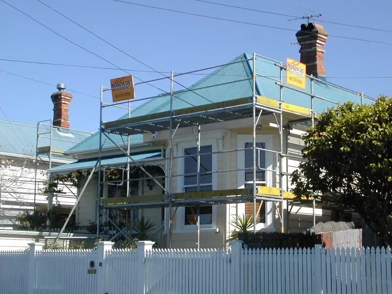 A house with scaffolding on the roof and a white picket fence