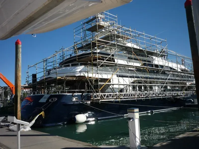 A large boat is docked in a harbor with scaffolding around it