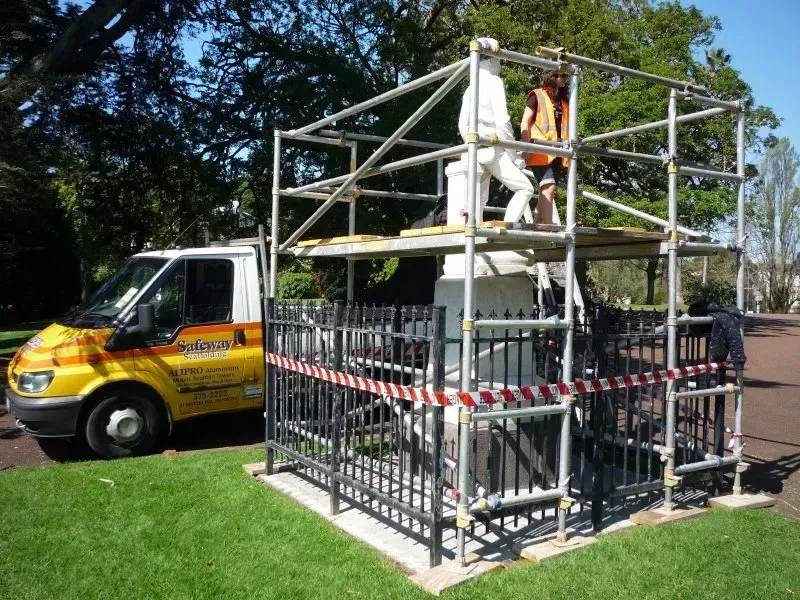 A yellow van is parked next to a fence and scaffolding