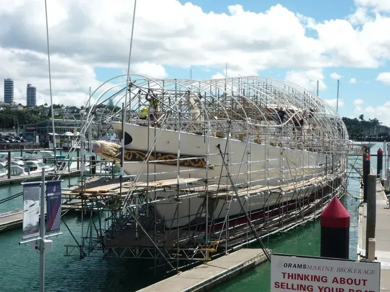 A boat is being built in a harbor with a sign that says thinking about selling your boat